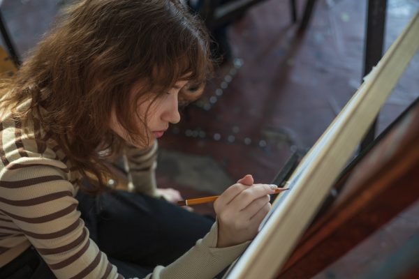 Ragazza artista in studio d’arte che disegna uno schizzo a matita su cavalletto. Ragazza artista in studio d’arte che disegna uno schizzo a matita su cavalletto.